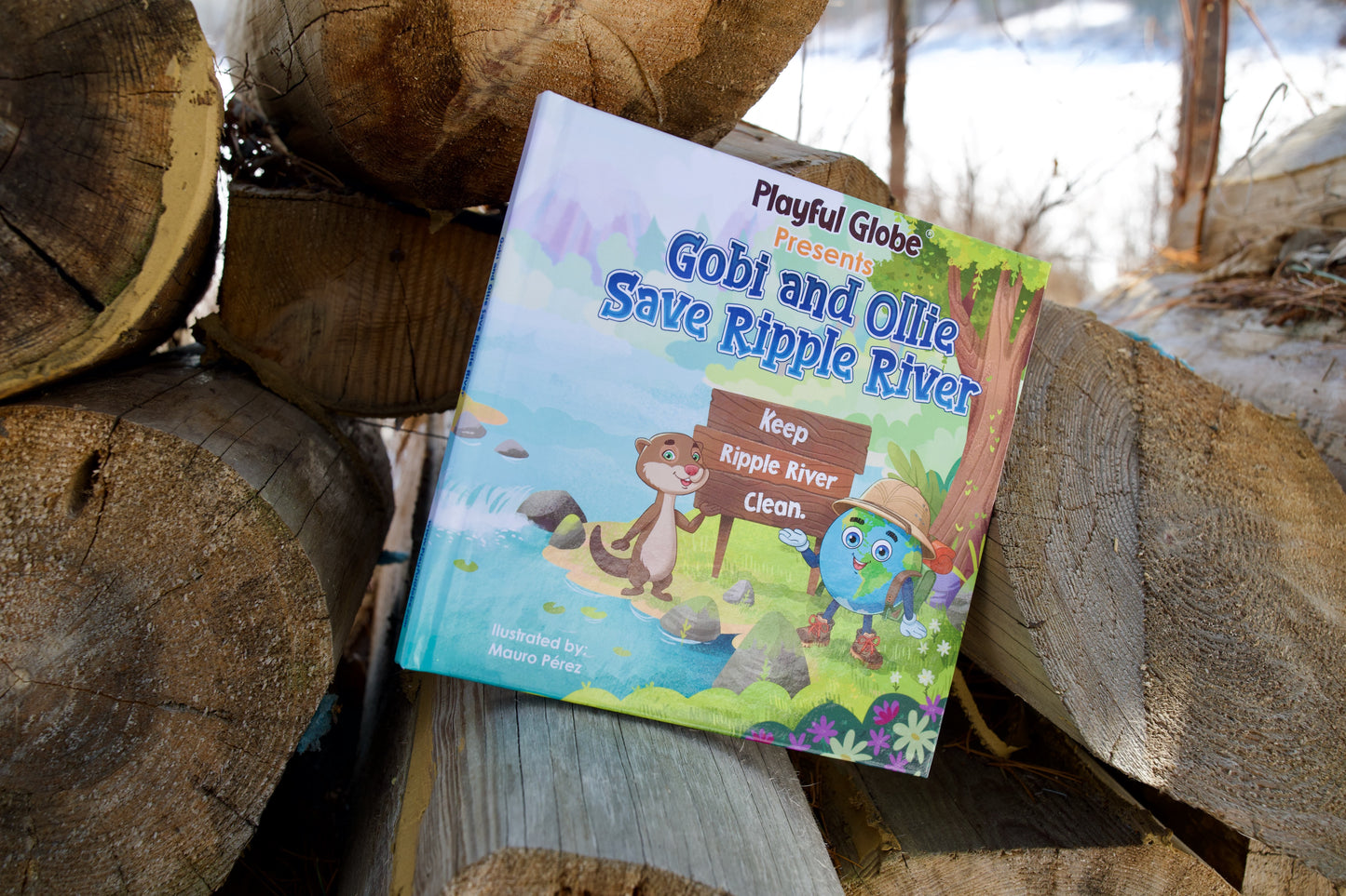 Children's book titled 'Gobi and Ollie Save Ripple River' on a stack of logs outdoors.