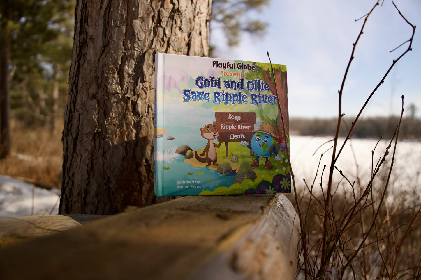 Children's book titled 'Gobi and Ollie Save Ripple River' leaning against a tree in a natural setting.
